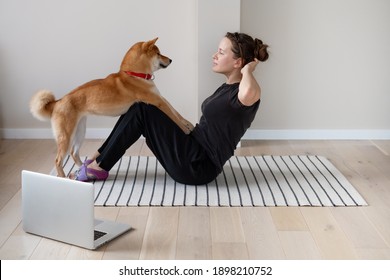 Young woman doing home strength training together with the help of her dog using online lesson - Powered by Shutterstock