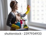 Young woman doing house chores. Woman holding cleaning tools. Woman wearing rubber protective yellow gloves, holding rag and spray bottle detergent. It