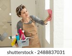 Young woman doing house chores. Woman holding cleaning tools. Woman wearing rubber protective yellow gloves, holding rag and spray bottle detergent. It