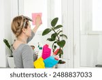 Young woman doing house chores. Woman holding cleaning tools. Woman wearing rubber protective yellow gloves, holding rag and spray bottle detergent. It