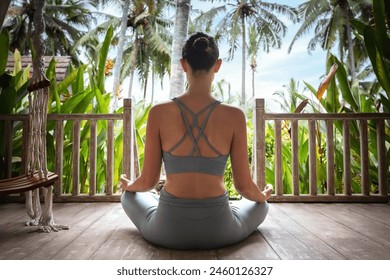 Young woman doing meditation in wooden porch in vacation summer resort. Rear view of young female meditating outdoors. Healthy lifestyle and mental health concept. - Powered by Shutterstock