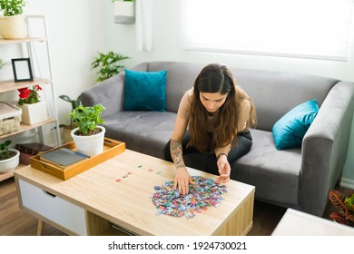 Young woman doing a mental health activity while resting in the living room. Hispanic woman putting together a jigsaw puzzle while sitting on the couch