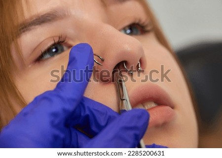 Young woman doing piercing nose ring at beauty studio salon