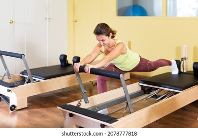 Young woman doing pilates exercises with a reformer bed