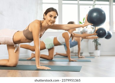 Young woman doing pilates with soft ball in female group in fitness studio