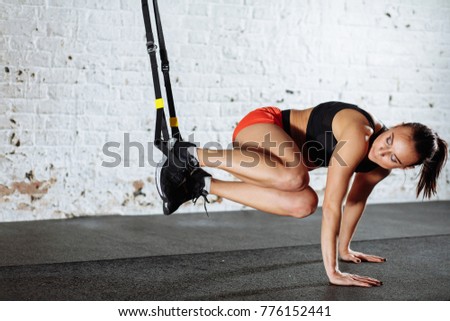 Young woman doing push-ups while legs hanging on trx