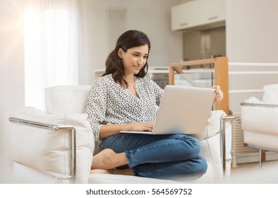 Young Woman Doing Research Work For Her Business. Smiling Woman Sitting On Sofa Relaxing While Browsing Online Shopping Website. Happy Girl Browsing Through The Internet During Free Time At Home.