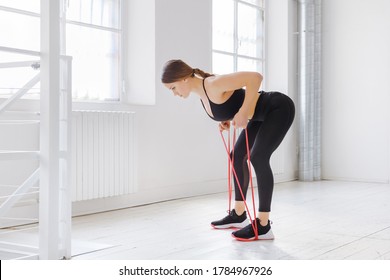 Young Woman Doing Rower Resistance Exercises With A Power Band In A Side View In A High Key Gym In A Health And Fitness Concept