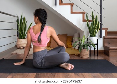 Young woman doing seated twist yoga pose at home. Active and healthy lifestyle.