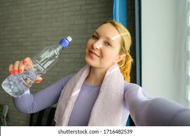 Young Woman Doing Selfies After Workout. Smiling Attractive Fitness Girl With Towel And Bottle Of Water After Training. Sport At Home During Lockdown.