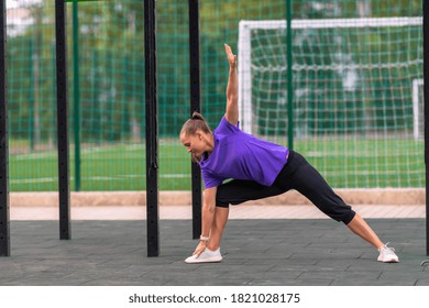 Young Woman Doing A Side Lunge And Stretch Yoga Pose At An Outdoor Sporting Facility With Sports Field In A Health And Fitness Or Active Lifestyle Concept