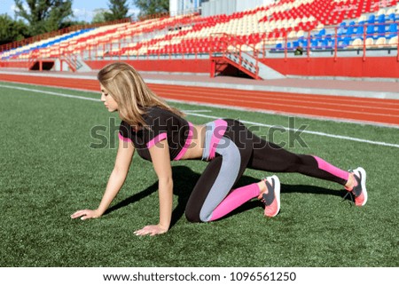 Young woman doing sports exercises on the grass at the stadium.