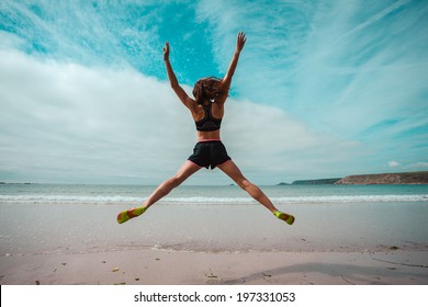 A young woman is doing star jumps on the beach by the sea