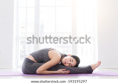 Young woman doing yoga childs pose, resting. stretching. Yogi workout on black mat on fitness class with windows, lifestyle healthy concept