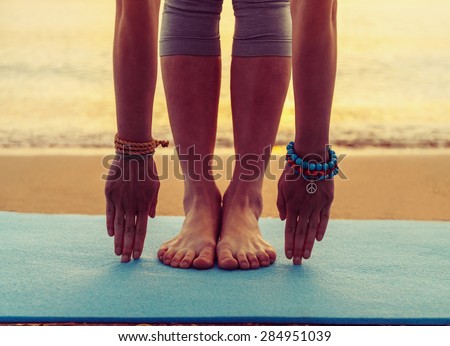 Young woman doing yoga exercise on beach near the sea at sunset in summer, face is not visible
