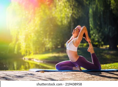 Young Woman Doing Yoga In Morning Park Near Lake 