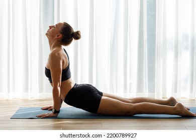 Young woman doing yoga vinyasa flow against big window with white curtains in the morning. - Shutterstock ID 2200789927