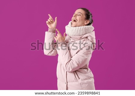 Young woman in down coat pointing at something on purple background