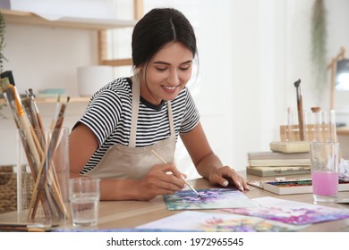 Young woman drawing flowers with watercolors at table indoors - Powered by Shutterstock