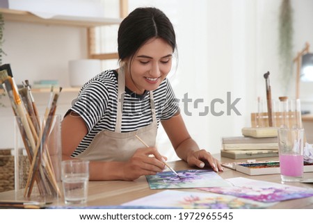 Young woman drawing flowers with watercolors at table indoors