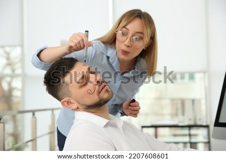 Young woman drawing on colleague's face while he sleeping in office. Funny joke