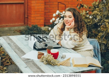 A young woman dreamily gazes into the distance while sitting at a table with a typewriter. Concept of a novelist.
