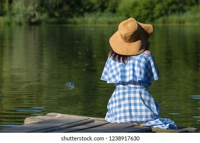 Young Woman In A Dress And A Straw Hat Blowing Bubbles Against T