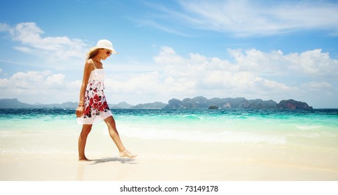 Young woman in dress and straw hat walking on beach