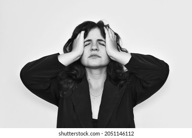 A Young Woman Dressed In A Black Jacket In A Bad Mood, Holding Her Head With Her Hands, Closing Her Eyes With A Sad Not Smile, Shows That She Is Very Tired And Worn Out.