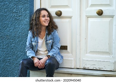 Young Woman Dressed In Black Leather Pants And Denim Jacket Sitting By A Door