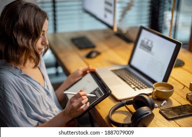 Young woman dressed casually having some creative work, drawing on a digital tablet, sitting at the cozy and stylish home office