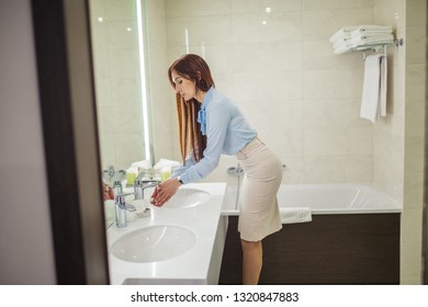 Young Woman Dressed In Formal Style Getting Ready For Work Doing Morning Hygienic Routine, Looking At Her Reflection In The Mirror While Washing Hands In The Bathroom