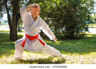 Young Woman Dressed In Kimono Practicing Her Karate Moves in park - red belt