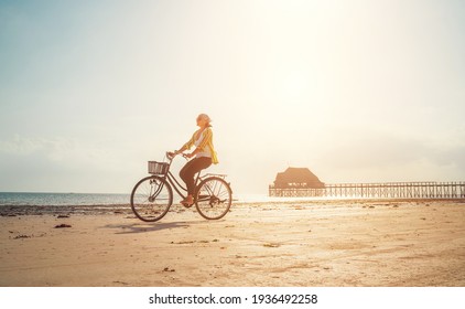 Young woman dressed light summer clothes riding old vintage bicycle with front basket on the lonely low tide ocean white sand coast on Kiwengwa beach on Zanzibar island, Tanzania. - Powered by Shutterstock