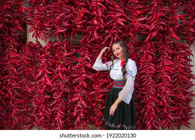 Young woman dressed on traditional Serbian Balkan clothing, national folk costume.Posing near of lot red paprika peppers