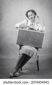 Young woman, dressed in retro style, sitting on a chair, with a suitcase on her knees. Studio black and white shot - Shutterstock ID 2074454941