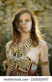 A young woman is dressed as Stone Age warrior. 
Her body and face is covered with mud and dirt.
She is seen posing in a stone quarry.