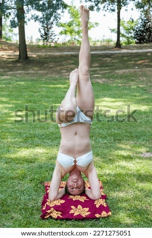 young woman dressed in a swimsuit does handstands in a public park