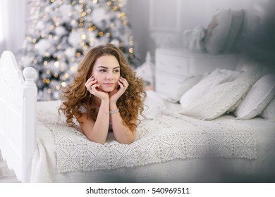 Young Woman In Dressing Gown On Background Of The Christmas Tree Lying On A Sofa, Morning Of The New Year