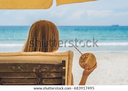 Young woman drinking coconut milk on Chaise-longue on beach