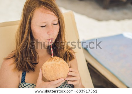 Young woman drinking coconut milk on Chaise-longue on beach. 