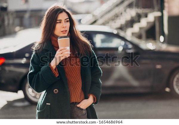 Young woman drinking\
coffee by her car