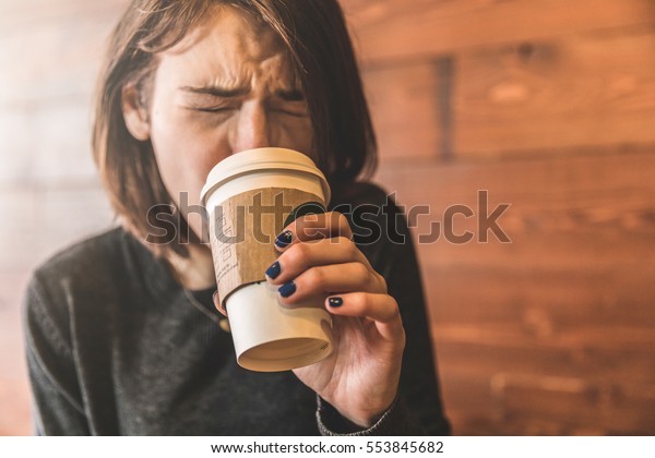 喫茶店でコーヒーを飲み グリマシンを飲む若い女性は 飲み物が熱くて舌を焦がすのです 短い髪の美しい白人の女の子は マグを持つ手にフォーカスする の写真素材 今すぐ編集
