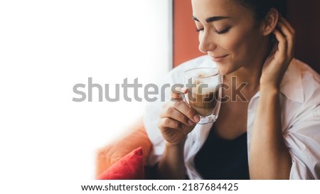 Young woman drinking coffee cappuccino sitting near window. Place for text.