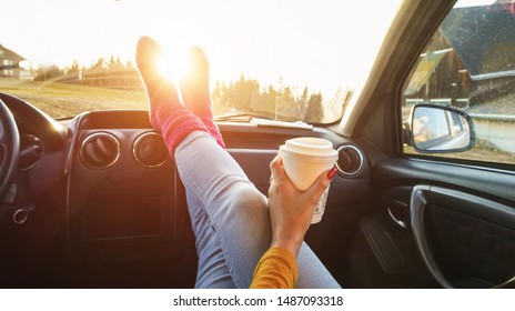 Young woman drinking coffee inside car in fall season - Girl relaxing and enjoying sunset traveling on europe mountains - Travel ,road trip and comfortable concept - Focus on paper hand
