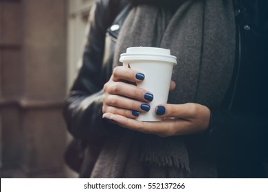 Young woman is drinking coffee on the street while walking on cold winter day. Close-up of hands with white take away cup of hot coffee. Copy-space blank for your advertisement text or design content