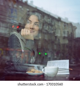 Young Woman Drinking Coffee And Reading Book Sitting Indoor In Urban Cafe. Cafe City Lifestyle. Casual Portrait Of Teenager Girl. Toned.