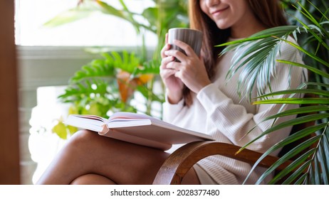 A young woman drinking coffee and reading book on balcony with houseplants garden at home