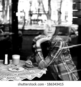 Young Woman Drinking Coffee And Use Her Smartphone Sitting Indoor In Urban Cafe. Cafe City Lifestyle. Casual Portrait Of Beautiful Girl. Black And White