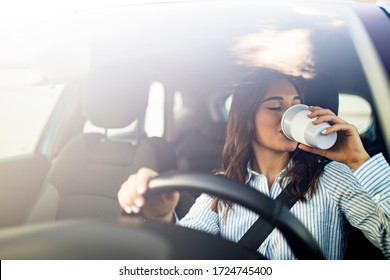 Young Woman Drinking Coffee While Driving Her Car. Photo Of A Smiling Business Woman In The Car Drinking Coffee. Making A Coffee Break. Businesswoman Dringking Cofee While Driving 